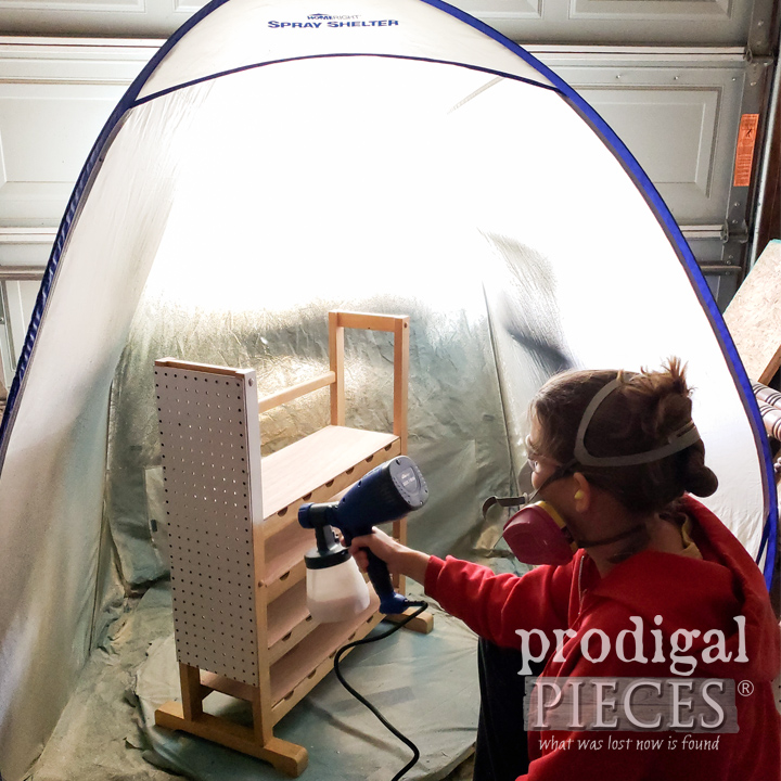 woman painting cart with paint sprayer in spray tent